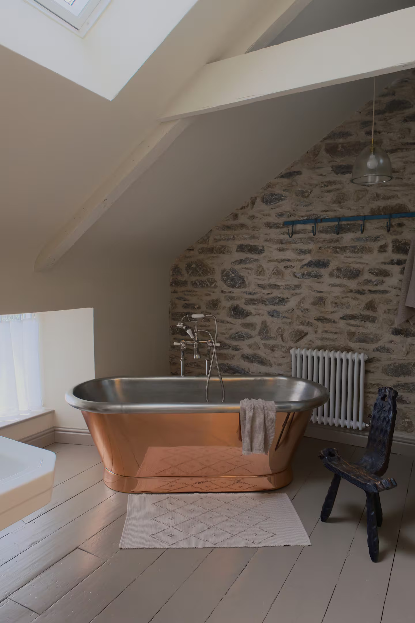 salle de bain mansardée avec poutres, baignoire en cuivre et mur de pierres décoration vintage salle de bain mansardée avec poutres, baignoire en cuivre et mur de pierres décoration vintage