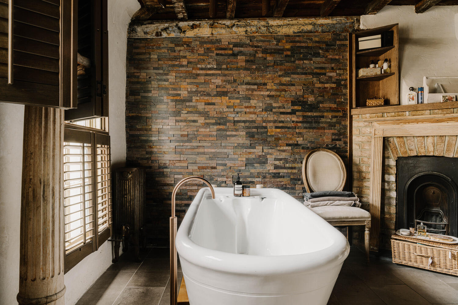 salle de bain rustique et moderne avec poutres cheminée briques anciennes et baignoire îlot